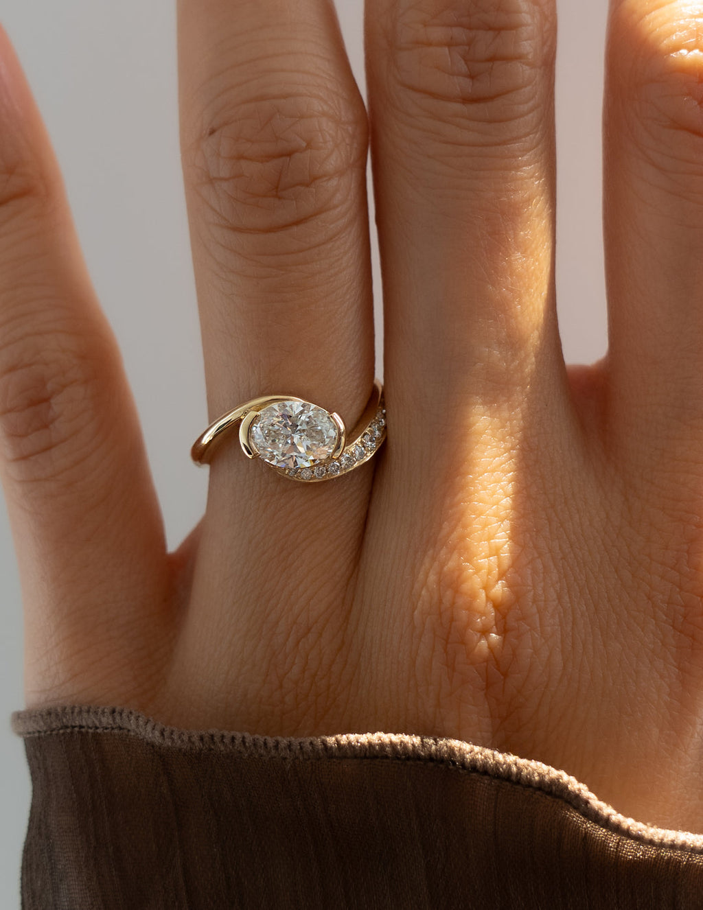Gold ring with a diamond on a person's finger against a neutral background