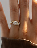 Gold ring with a diamond on a person's finger against a neutral background